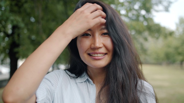 特写的亚洲妇女看镜头微笑触摸头发在公园视频素材