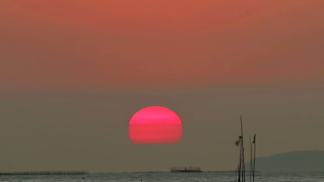 夕阳下，红彤彤的天空落在云上，海面上渔船在流逝时光视频素材