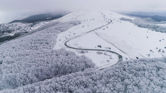 冬季空中公路旅行。无人机飞越白雪皑皑的山脉，在冬季的大雾天气中景观。视频素材