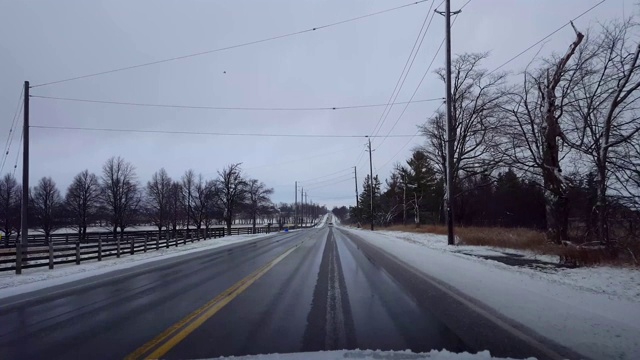 驾驶在冬天的乡村道路与雪在道路的一边在白天。司机的观点POV驾驶街道与雪在树上与阴云天空。视频素材