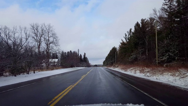 驾驶在冬天的乡村道路与雪在道路的一边在白天。司机的观点POV驾驶街道与雪在树上与阴云天空。视频素材