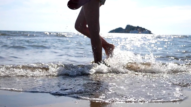 女性的脚走在海水上的海滩与海景和波浪的背景。年轻女子的双腿沿着海岸行走。赤脚女孩在海边漫步。暑假或旅游概念。视频素材