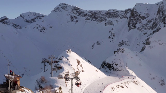 滑雪缆车移动与滑雪者在雪山度假村鸟瞰图。冬季滑雪场雪坡上乘坐滑雪电梯的乘客。无人机在滑雪胜地观看冬季活动视频素材