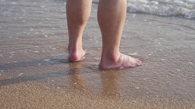 海浪触摸脚在沙子和大海，两脚站在海滩上视频素材