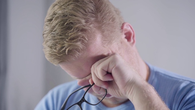 特写疲惫的红发白人男子摘掉眼镜，揉眼睛。精疲力竭的商人努力工作。超负荷工作、生活方式。视频素材