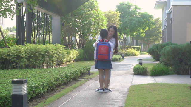 亚洲女孩学前班的学生跑到妈妈的手拥抱她后，在房子在村庄的房子前。为人父母或爱与联结的表达概念。视频素材