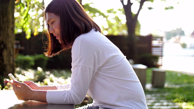 日落时分，一名女子在户外公园使用手机视频素材