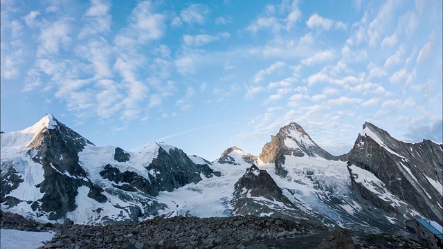 月光和明媚的阳光下，雪山、木屋和散步的人的全景。间隔拍摄视频素材