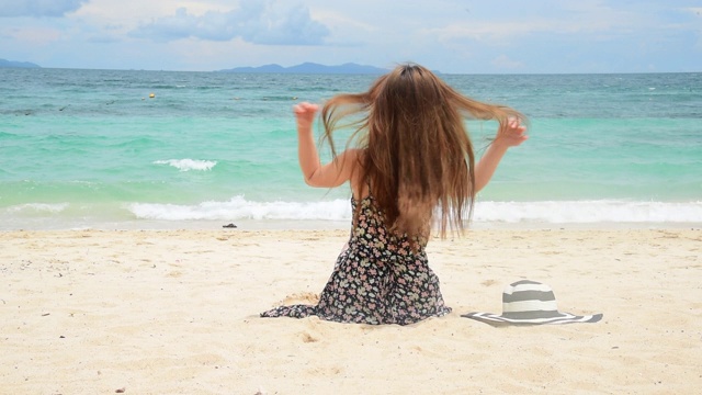 夏天的时候，在海滩上晒太阳的女人度假。快乐的女人穿着夏装，戴着草帽坐在海滩上看海。夏季休闲生活方式户外拍摄热带岛屿海滩。视频素材