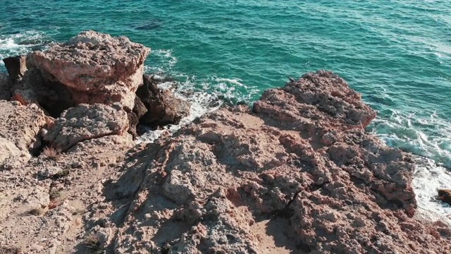 鸟瞰图的岩石海岸。美丽的海岸线，蔚蓝的海水。海浪撞击悬崖。浪花溅起并产生泡沫。无人机拍摄的海洋巨石。湛蓝清澈的海浪视频素材