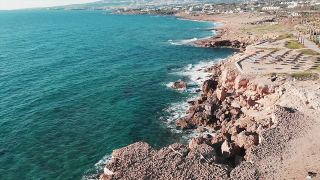 海浪拍打着海滩上的岩石峭壁。鸟瞰图的岩石海岸。鸟儿飞过海岸线。无人机拍摄塞浦路斯岛。帕福斯的旅游区视频素材