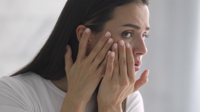 忧心忡忡的女人看着镜子，检查眼睛区域的皱纹。视频素材