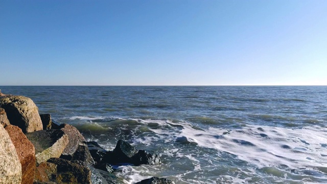 光波拍打着岩石的海岸，水面上泛起白色的泡沫。海边的晴天。水在石头周围流动视频素材