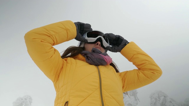 一个年轻女人的特写肖像把她的滑雪眼镜在雪上在一个滑雪胜地。赏冬山。准备在白雪皑皑的山上滑雪。下坡滑雪。视频素材