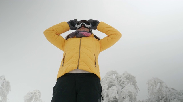 一个年轻女人的特写肖像把她的滑雪眼镜在雪上在一个滑雪胜地。赏冬山。准备在白雪皑皑的山上滑雪。下坡滑雪。视频素材