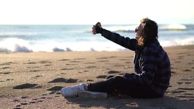 一个年轻人在海滩上玩手机视频素材