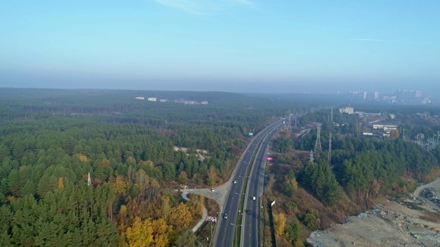 空中无人机视频。飞过森林附近的高速公路，地平线上有城镇。视频素材