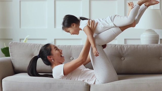 快乐的亚洲妈妈在沙发上玩抬小孩的女儿视频素材