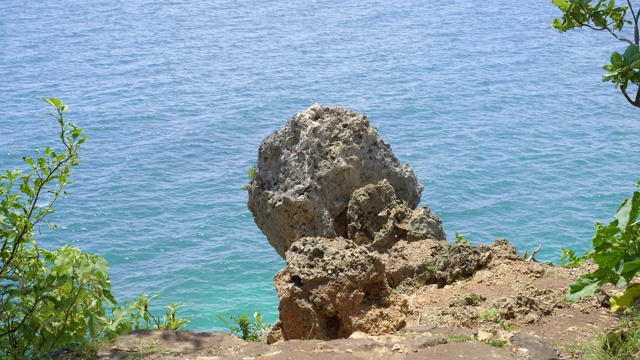 在充满活力的蓝色海洋的岩石海滩上，一块巨大而锋利的石头视频素材