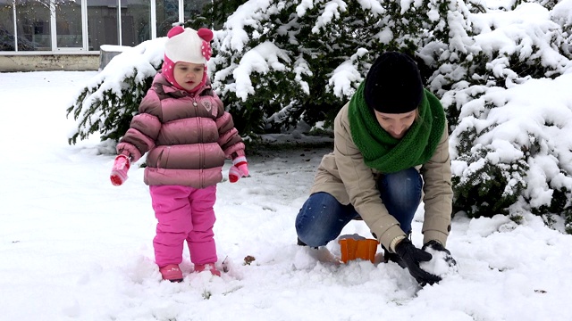 女人带着女儿扔雪球。幸福的家庭的女孩。雪落视频素材