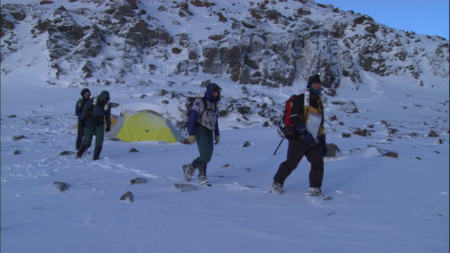 登山队员们离开帐篷，徒步穿越雪地。视频素材