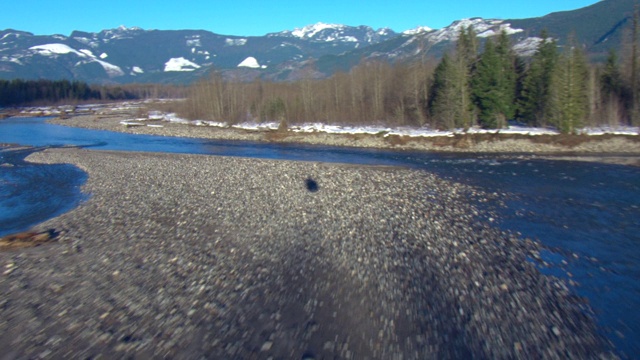 一架直升机飞过群山附近一片覆盖着积雪、灌木和湿地的广阔景观。视频素材