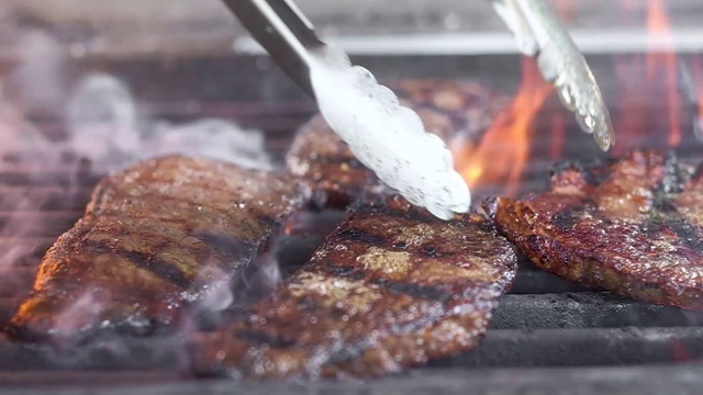 主任用钳子转动烤架上的肉。多汁、肥美的油炸肉。牛肉在大火上炸。画面里有很多火和烟。慢镜头特写视频素材