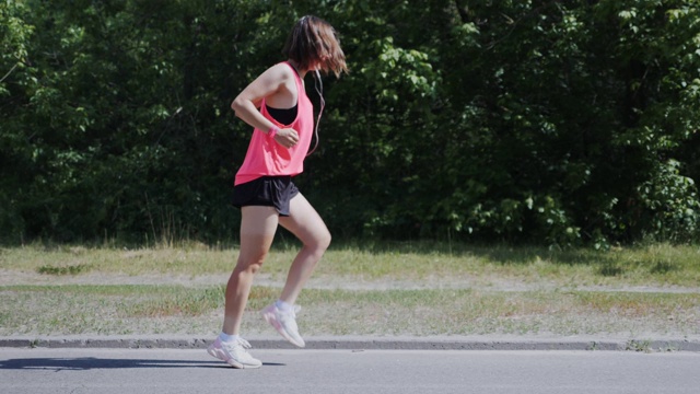 迷人的运动女孩在公园跳舞。年轻女孩表演滑稽的舞蹈和胡闹。可爱的女孩穿着粉红色的衬衫笑着玩。慢动作视频素材