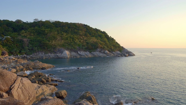 在温暖的夕阳下，有巨石的海滩、小山和森林视频素材