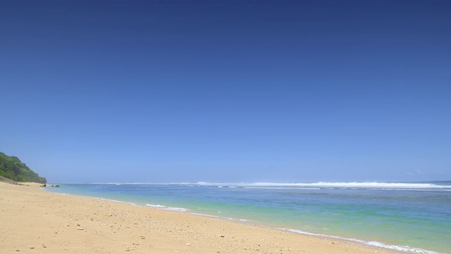 阳光明媚的热带海滩，黄色的沙子和石头，美丽的彩色海洋与大潮汐波浪靠近礁石视频素材