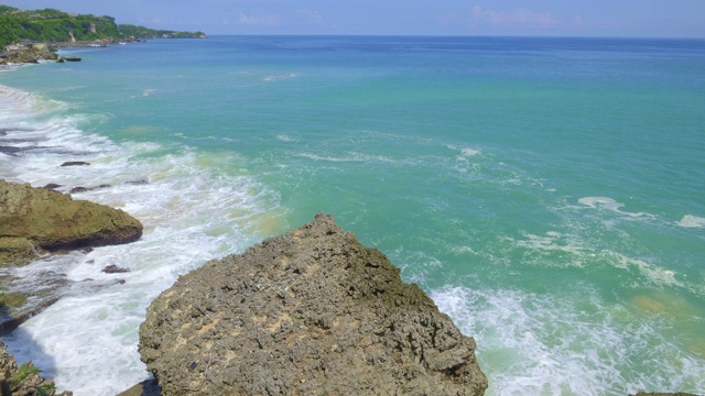 在阳光明媚的日子里，热带岛屿上有美丽的蓝色海水和巨浪的岩石海滩的慢镜头视频素材