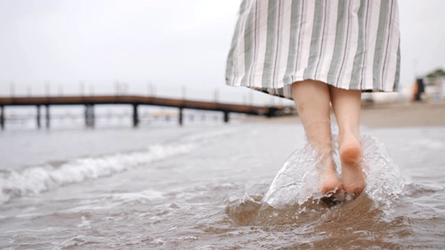 女性徒步旅行者的脚赤脚在海滩上日落。年轻女子的双腿在海边漫步。视频素材