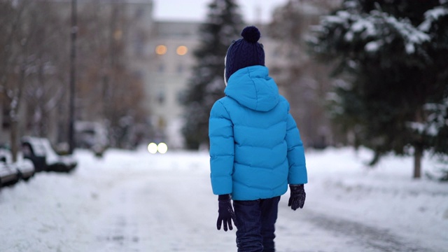 可爱的四岁男孩穿着蓝色冬装走在覆雪街道视频素材