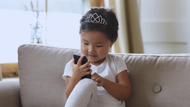 好奇的小亚洲女孩独自坐在沙发上使用智能手机视频素材