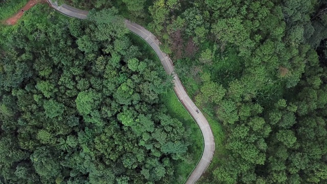 一辆摩托车行驶在公路上的鸟瞰图穿过绿色森林在泰国清莱省的高原山区。视频素材