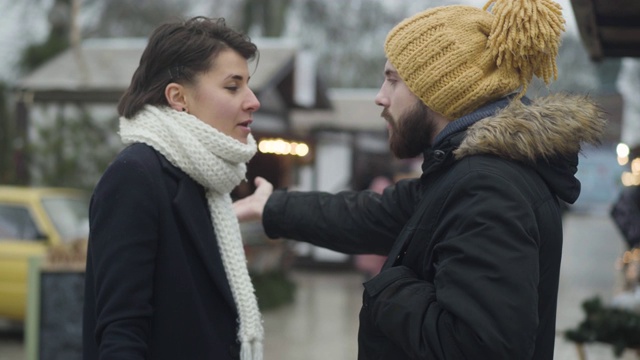 一个年轻白人家庭在户外争吵的侧面。美丽的黑发女子和留胡子的英俊男子谈话和手势作为情感站在冬天的街道。通信问题。视频素材