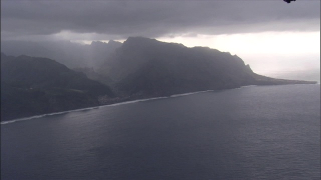 一架飞机朝笼罩在多山海岸上空的暴风云飞去。视频素材