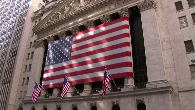 宽街站的地铁台阶对面的纽约证券交易所(New York Stock Exchange)上悬挂着一面美国国旗。视频素材