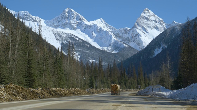 载着圆木的汽车和卡车沿着雪山下的道路行驶视频素材