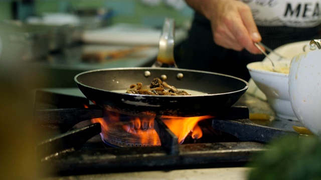 在一家户外餐厅，厨师用高温煎锅准备蘑菇意大利面。视频素材