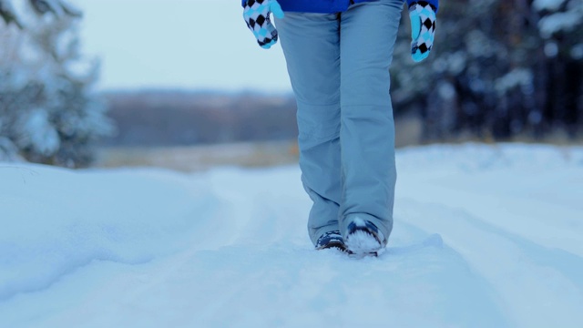 雪地里，一个女人穿着冬天的鞋走在雪地上。冬天在树林里的雪地里散步。特写镜头。视频素材