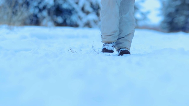 那家伙穿着冬靴在雪地里走。沿着森林小径走，踏在雪地里。特写镜头。视频素材