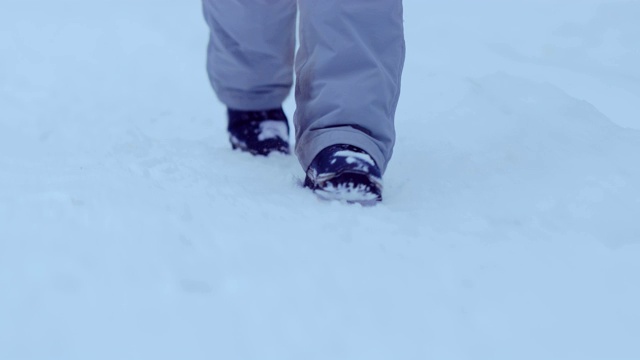 穿着冬靴的双腿走在雪地上。冬天走，踏在雪里。特写镜头。视频素材