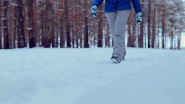 一个女人走在白雪覆盖的森林小路上，双腿穿着冬靴走在雪道上。特写镜头。视频素材