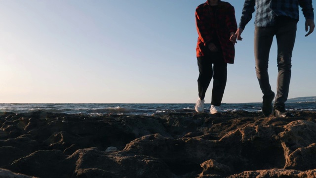 日落时分，一个年轻人牵着女朋友的手走在海滩上。男人和女人在海滩上享受大海。夕阳下，一对情侣沿着海边散步的剪影。浪漫的海滩之夜视频素材