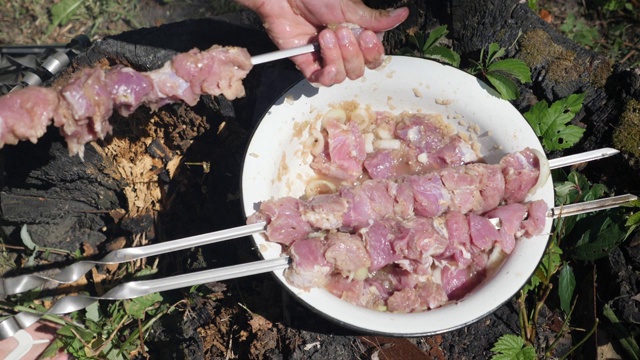 男人把生肉串在烤肉串上。准备烤肉。户外烧烤。油炸肉类的烹饪过程视频素材