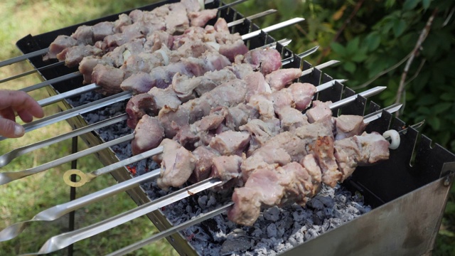 生肉串上，近景。烤肉片。室外烧烤。准备食物的过程。男人翻着腌肉视频素材