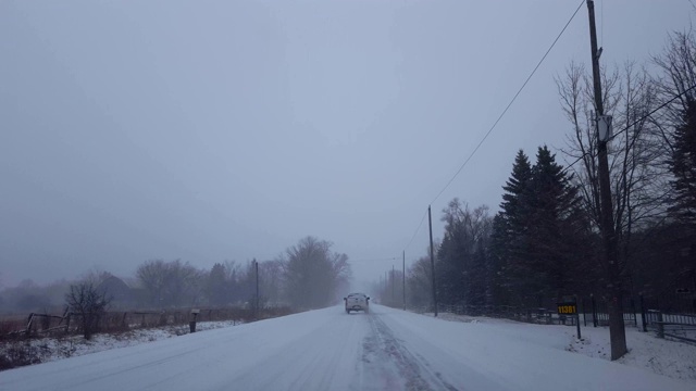 在路边有常绿树木的乡村道路上驾驶，在车辆后面行驶。下雪时，卡车后面的司机视角。视频素材