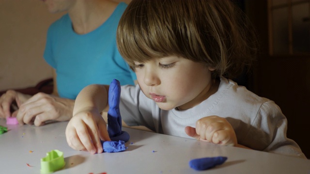 儿童在幼儿园的桌子上塑橡皮泥的过程。孩子和妈妈在家里的游戏室玩彩色的粘土玩具。年轻女子和儿子在托儿所玩彩色粘土。视频素材