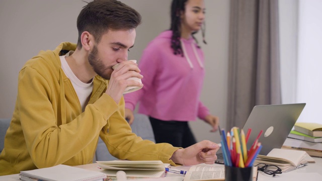 迷人的非洲裔美国女孩带来一杯茶或咖啡的年轻白人男孩坐在桌子上阅读和写作。学生互相帮助学习。教育、生活方式。视频素材